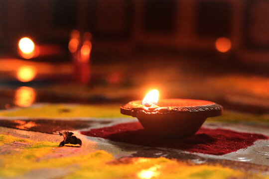Traditional Clay Diya Oil Lamp Glowing on Colorful Rangoli Design, Warm Festive Lighting for Diwali Celebration, Hindu Festival of Lights Background, High Resolution Stock Photo