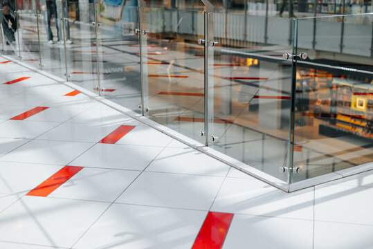 bright retail area featuring a glass railing and a floor design with bold red markings. Bright lights reflect off the surfaces, creating a lively shopping atmosphere