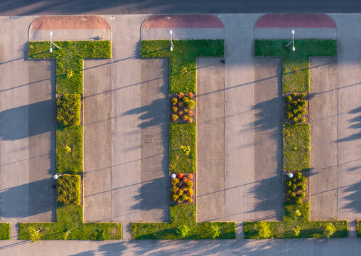 Aerial view of the Morasko Campus parking lot featuring geometric green strips, manicured shrubs, and trees casting long shadows in Poznan, Greater Poland Voivod, Poland.