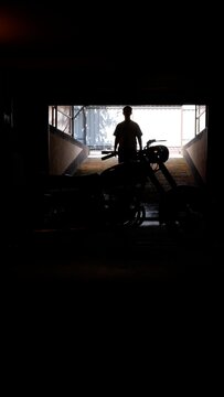 Man with a motorcycle standing in silhouette against a bright outdoor opening, creating a strong contrast when entering a dark, mysterious garage or tunnel