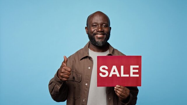 Portrait of African American man holding sale sign, pointing at banner and gesturing thumbs up. Clip suits retail marketing campaigns and commercial discount promotions