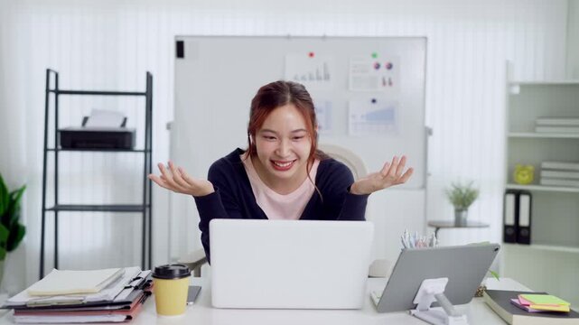 Young Asian businesswoman smiling during video call on laptop in bright hybrid work office