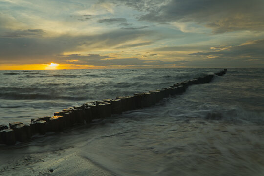 Malerischer Ostsee-Sonnenuntergang mit h&ouml;lzernen Buhnen und flie&szlig;endem Wasser
