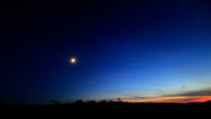 Moon on a twilight sky with stars, planets and landscape mountain silhouettes. © astrosystem