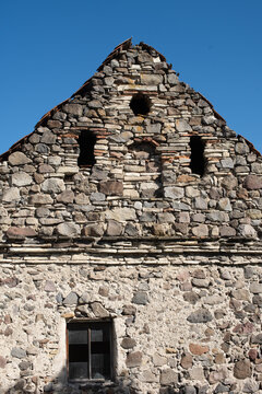 Historic stone building with weathered masonry, rustic architecture, small openings and textured walls against a vivid blue summer sky.