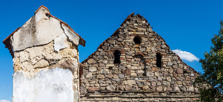 Historic stone building with weathered masonry, rustic architecture, small openings and textured walls against a vivid blue summer sky.