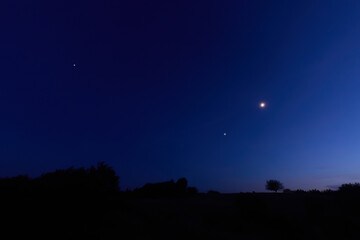 Moon on a twilight sky with stars, planets and landscape mountain silhouettes. © astrosystem