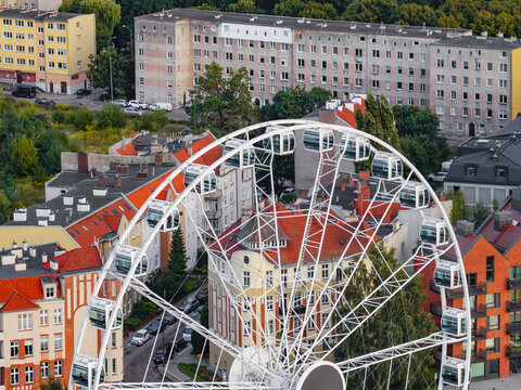 Aerial view of a large Ferris wheel set against a backdrop of historic red-roofed buildings and modern residential architecture in Gdansk, Pomeranian Voivodeship, Poland.