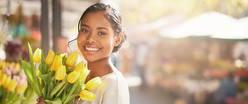 Smiling woman holding yellow tulips bouquet with blurred outdoor flower market background banner.