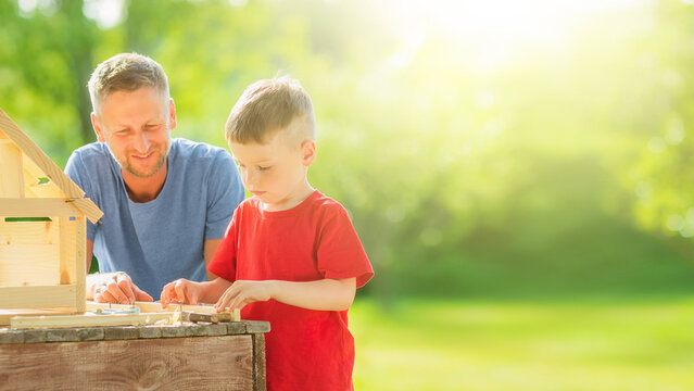 Father and son building wooden birdhouse together with blurred sunny backyard background banner.