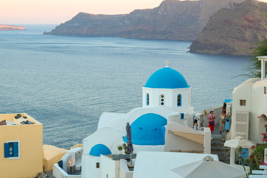 View of Santorini, Greece with blue dome churches and cliff views of houses and businesses overlooking the caldera. Famous tourism destination.