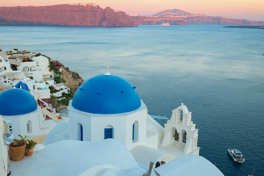 View of Santorini, Greece with blue dome churches and cliff views of houses and businesses overlooking the caldera. Famous tourism destination.