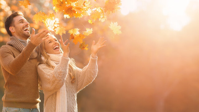 Happy young couple throwing golden autumn leaves with blurred sunny park background banner.