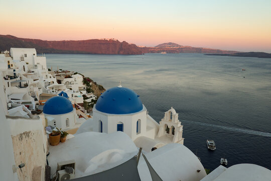 View of Santorini, Greece with blue dome churches and cliff views of houses and businesses overlooking the caldera. Famous tourism destination.
