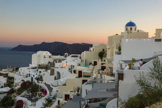 View of Santorini, Greece with blue dome churches and cliff views of houses and businesses overlooking the caldera. Famous tourism destination.