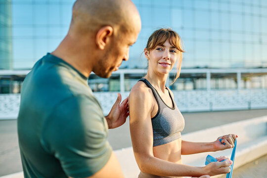 Portrait of a happy beautiful woman exercising with resistance band  and stretching with trainer coach support outdoors