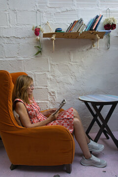 Mature woman reads a magazine in a colorful boho armchair at a rustic guesthouse in Colombia, capturing the slow pace and quiet comfort of unplugging while traveling