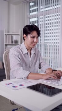 Young Asian professional working on laptop at home desk analyzing charts during hybrid workday