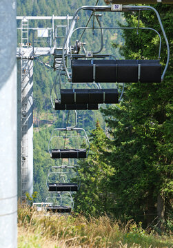 Empty chairlift seats follow each other along a forested mountain slope. Repeating chairs create strong visual depth.