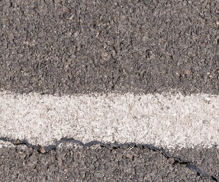 Asphalt road marking with a worn white painted line, showing a weathered grey pavement texture for industrial and design backgrounds