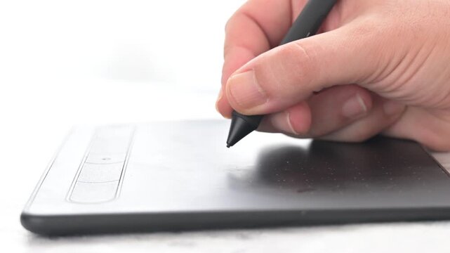 Man's Hand uses a stylus pen on a graphic tablet to draw design or retouch images on a computer in a digital creative workspace.
