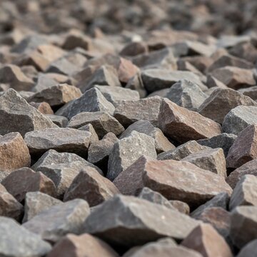 Close up of crushed grey and brown granite stones for construction and landscaping, showing detailed texture and sharp edges with shallow depth of field, concept of durability and raw foundation