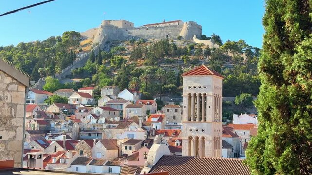 Fortress on a hill overlooking a coastal town with traditional architecture and greenery in the foreground in Hvar, Croatia 