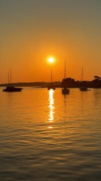 View from bow of sailing yacht anchored in quiet bay during golden sunset with other boats in distance. Concept of slow travel, sailing adventure, anchoring, freedom and peaceful evenings on water