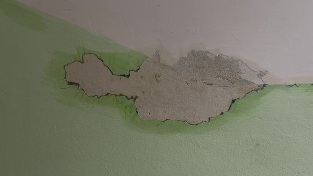 Close-up of peeling green paint and damaged plaster on a house wall caused by water leakage or high humidity.