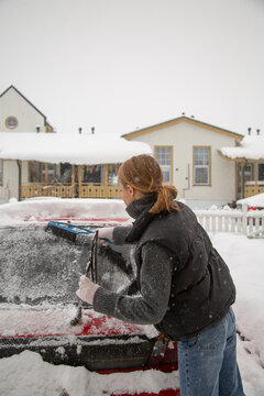 Woman clearing snow and ice from car windshield