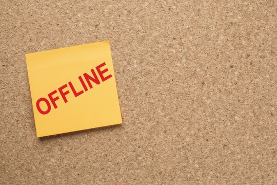 Yellow sticky note with the word offline written in red on a cork board