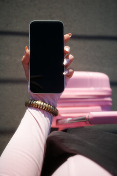 Hand showing blank phone screen beside pink luggage
