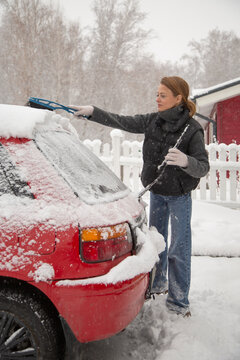 Woman clearing snow off red car in winter