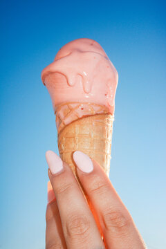 Melting pink ice cream cone held against clear blue sky
