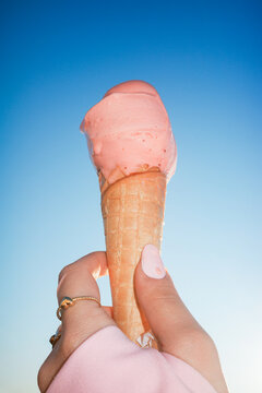 Hand holding melting strawberry ice cream against clear blue sky