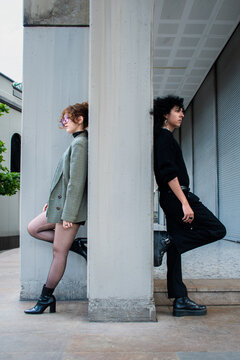 Two People Pose Near a Concrete Column on a City Street