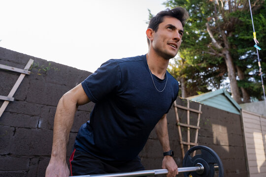 Young man doing bend-over rows using a barbell in the backyard