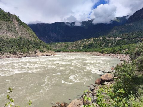 Rushing grey water of the Yarlung Tsangpo river between rocky banks and forested mountains in Nyingchi, Xizang, China