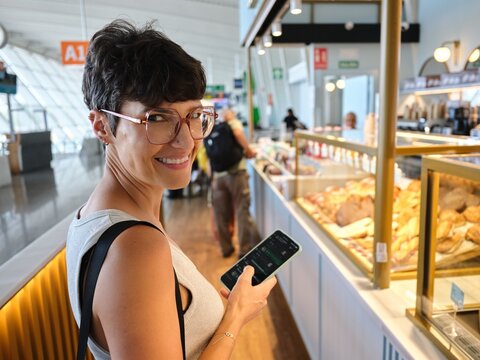 Woman smiling while using smartphone in airport cafe