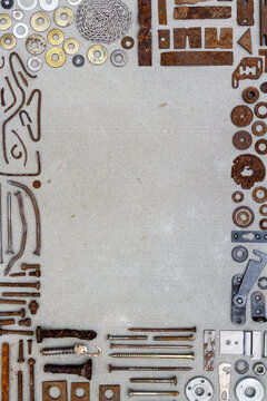 A frame of various old rusty bits and pieces arranged on a concrete surface. Old rusty nuts, bolts, nails and other parts flay lay on gray background.