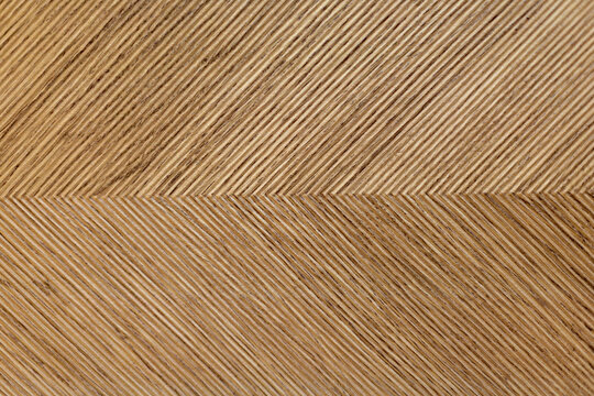 Ribbed Wood Surface with Chevron Pattern. Close view of brown wood with fine diagonal grooves forming a repeating chevron pattern.