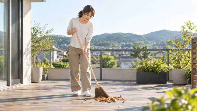 早朝の住宅テラスで落ち葉を掃除する日本人女性