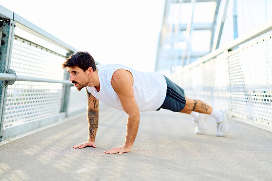 Fit man doing push-ups on a modern city bridge, engaging in an intense outdoor workout for strength and fitness