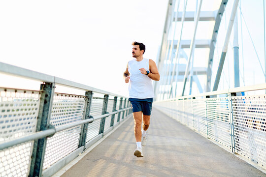 Athlete performing an outdoor workout, jogging across a contemporary bridge structure, embodying a healthy lifestyle and endurance