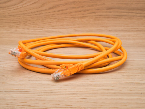 Orange Ethernet Cable on Wood - A coiled orange ethernet LAN network cable with two RJ45 connectors rests on a light wooden background.