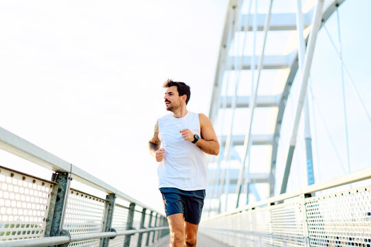 Man running on a modern bridge, staying active and healthy in an urban environment with a smart watch