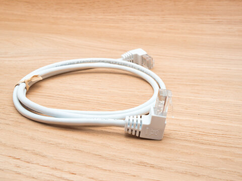 White Ethernet Network Cable on Wood - A coiled white Cat 5e UTP Ethernet network cable with RJ45 connectors lies neatly on a light wood grain surface.
