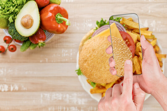 Hands photograph a burger on a phone beside a bowl of fresh produce