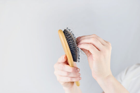 Hands pull shed dark hair from a wooden hairbrush in a studio