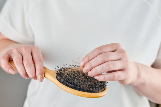 Person holds a wooden hairbrush packed with shed light brown hair